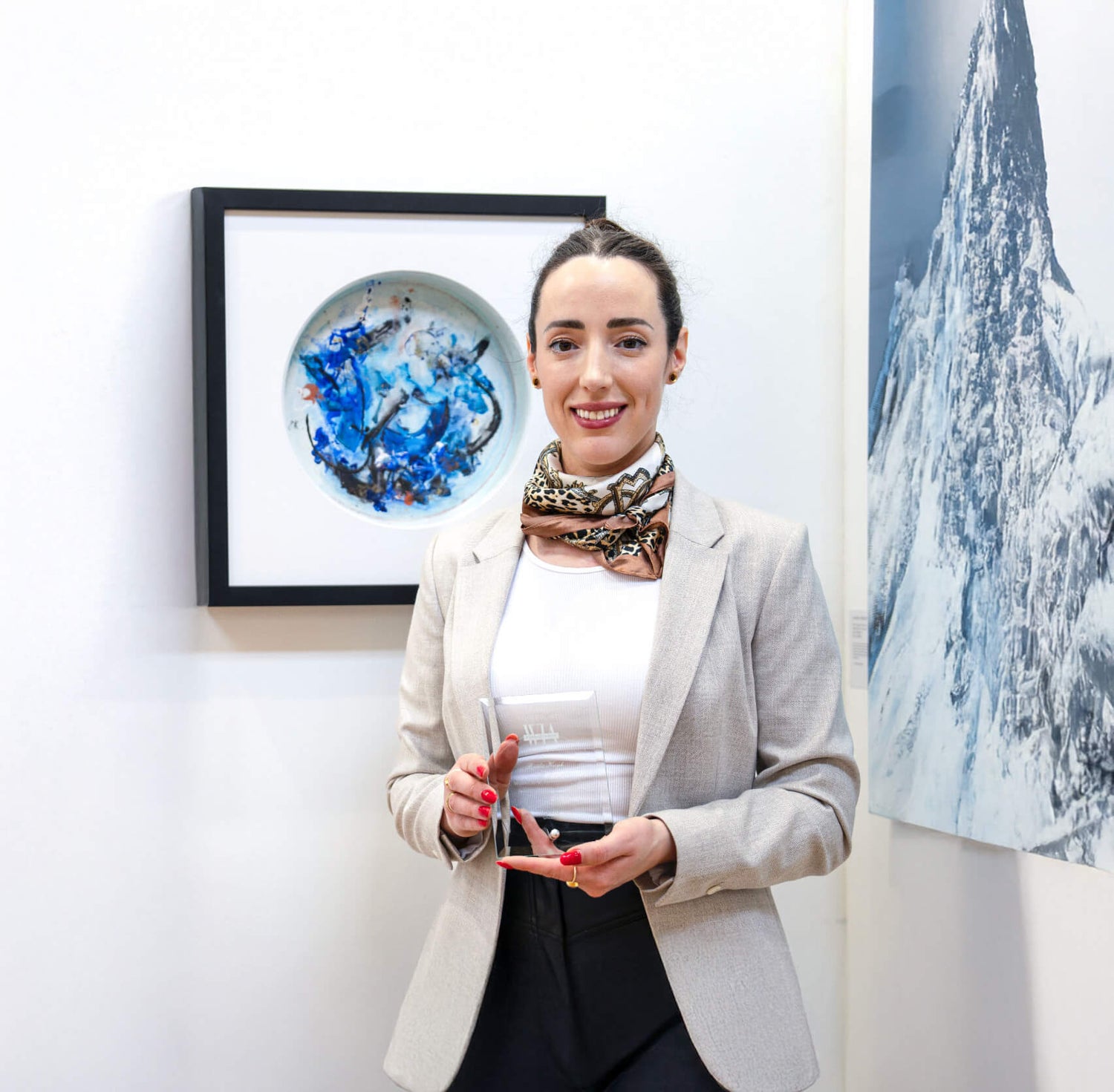 Irish artist Bridie Keogh at the Women in art Biennale in London holding her award with her framed statement abstract artwork on the wall behind 