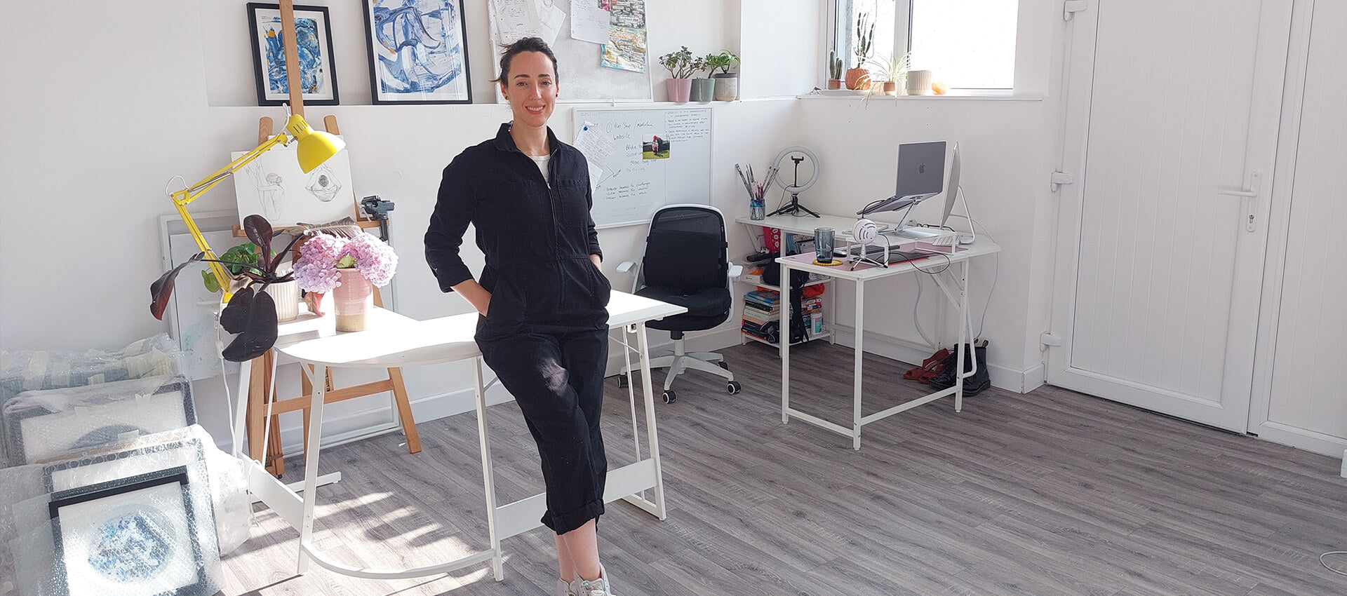 Irish artist Bridie Keogh in her art studio space with white walls and wooden flooring and art behind her