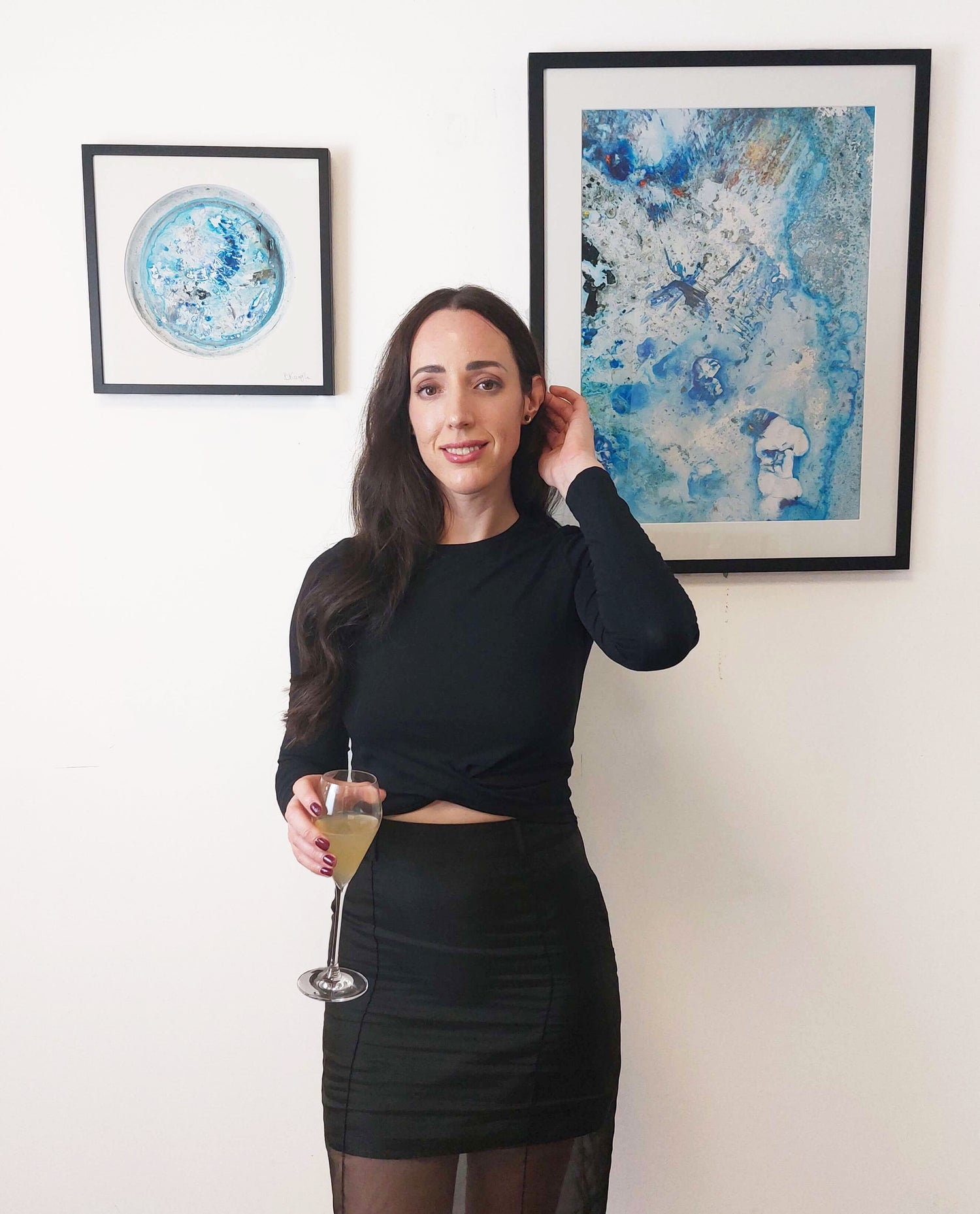 Irish artist Bridie Keogh in a black outfit holding a drink in front of her abstract art on a wall at a gallery exhibition